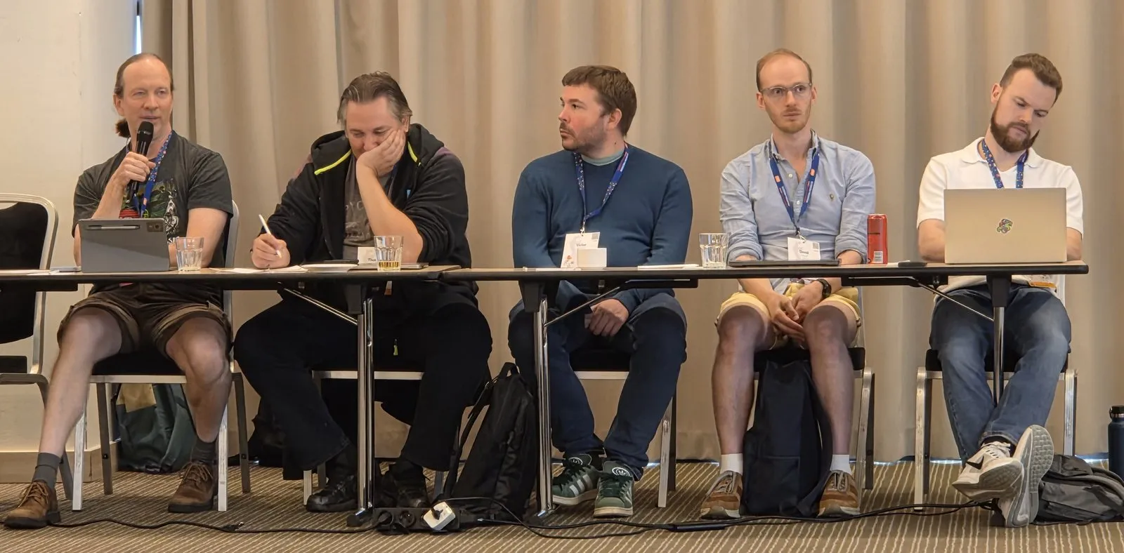 Gregory P. Smith speaking into a microphone, seated in a row of attendees
