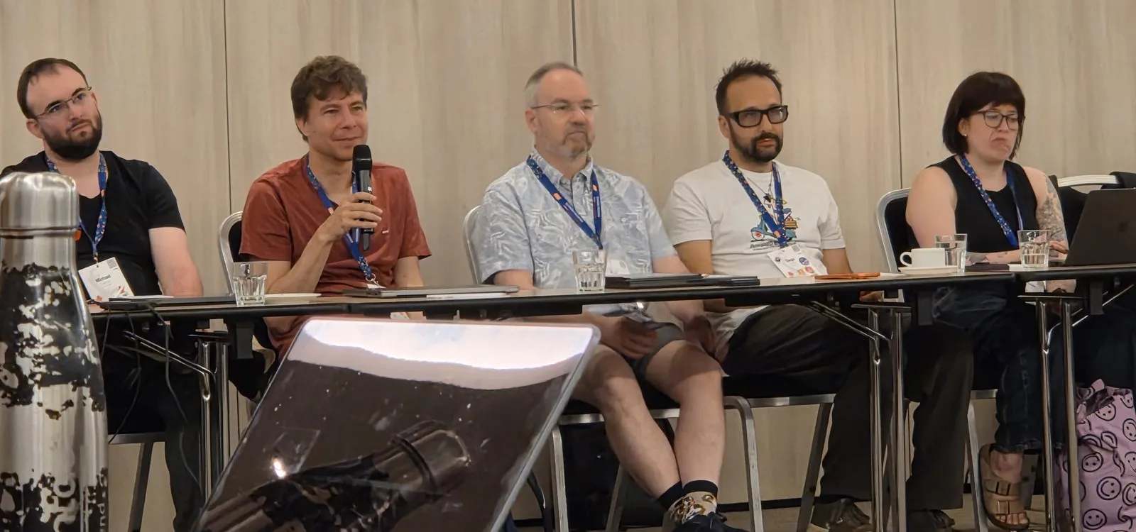 Jukka Lehtosalo speaking into a microphone, seated in a row of attendees