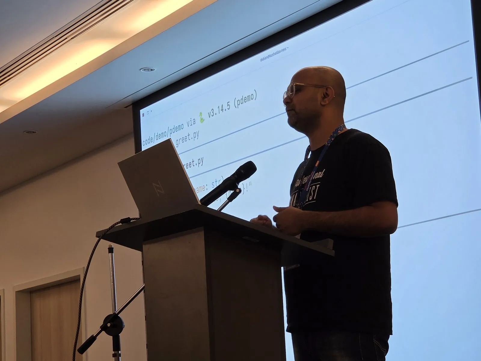 Kushal Das at the lectern, with his demo terminal projected on the screen behind him